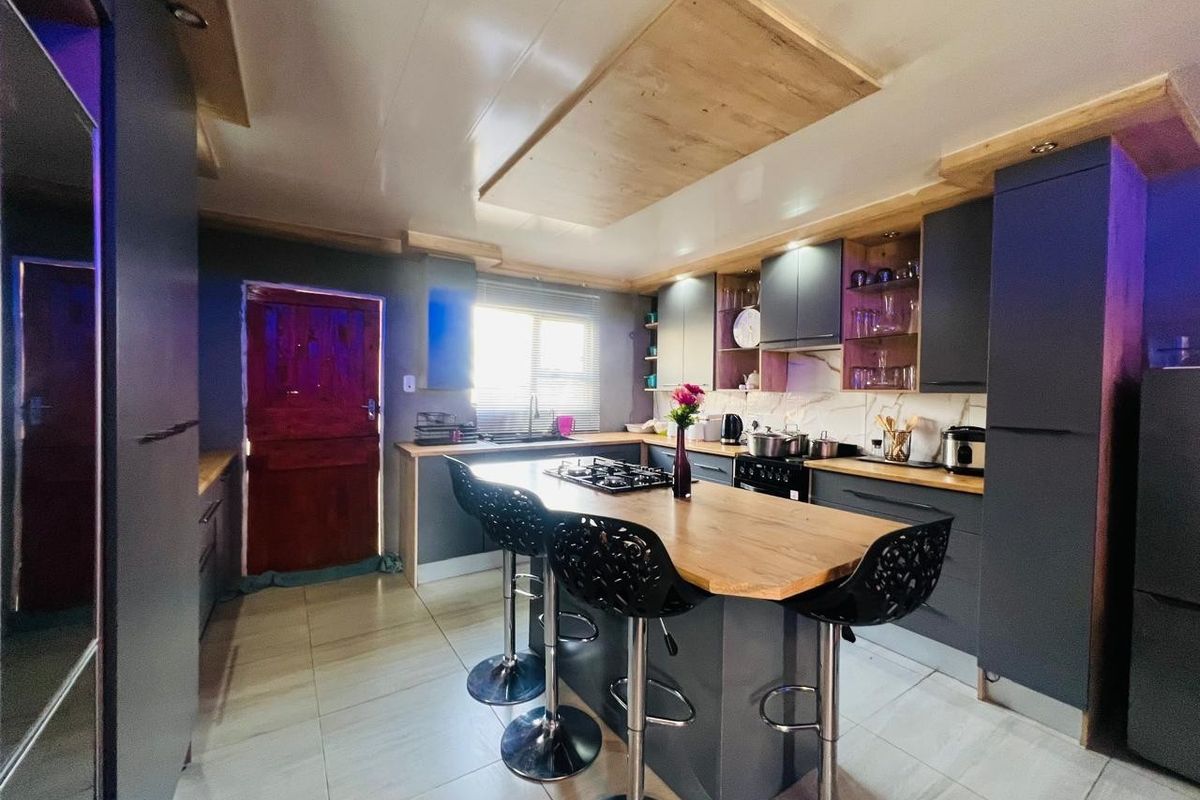 Modern kitchen featuring dark cabinetry, a central island with a gas hob, stone countertops, and tiled flooring with unique ceiling detailing.