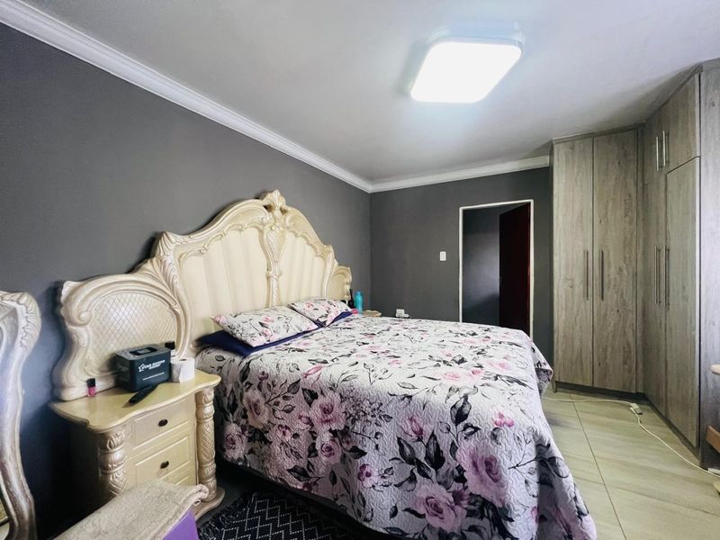 A well-maintained bedroom featuring built-in cupboards, decorative ceiling cornicing, and neutral tiled flooring.