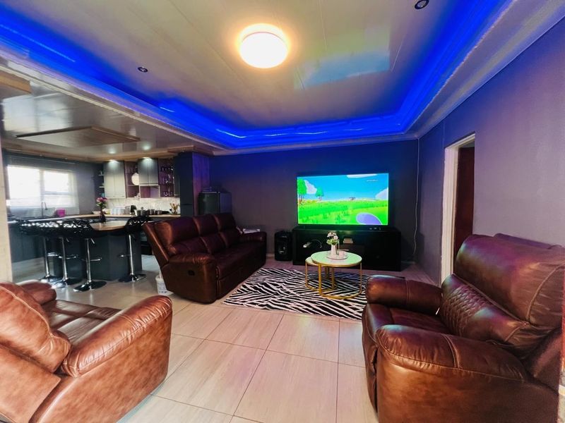 Open-plan living area featuring tiled floors, recessed ceiling lighting with blue accent strips, and an integrated kitchen with a breakfast bar.