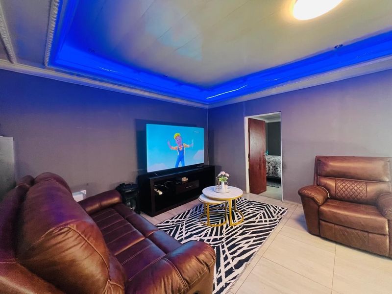 A living room featuring a recessed ceiling with integrated blue LED accent lighting and tiled flooring.