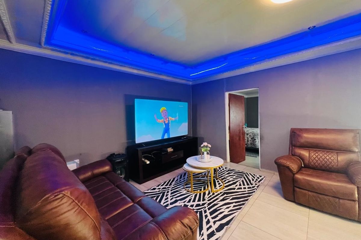 A living room featuring a recessed ceiling with integrated blue LED accent lighting and tiled flooring.