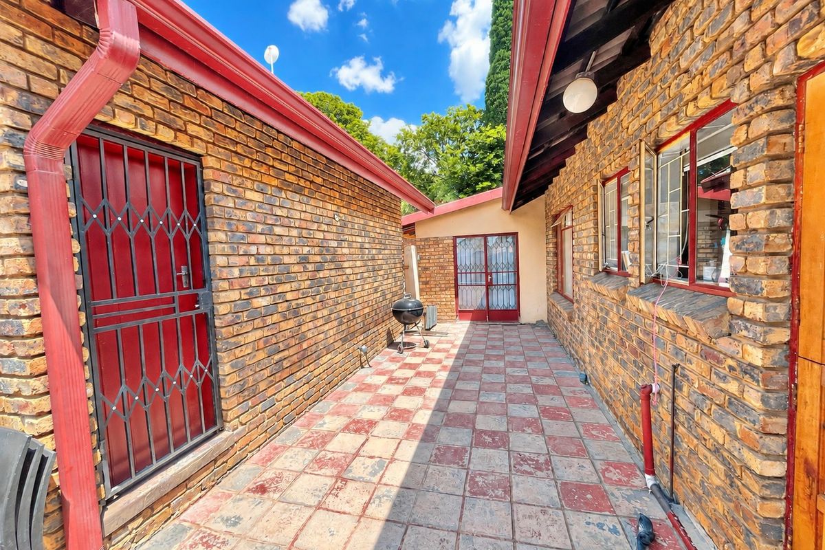 A paved rear courtyard area featuring face brick walls, security gates, and metal window frames, providing a functional outdoor space between building sections.
