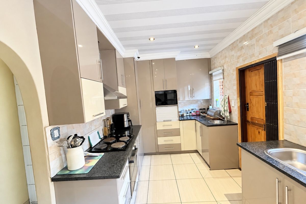 Modern kitchen featuring high-gloss cabinetry, granite countertops, integrated electric hob and oven, tiled backsplash, and double sink with ample storage space.