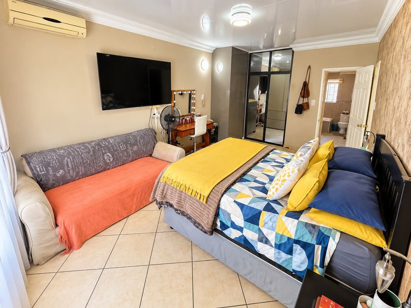 Spacious bedroom featuring tiled flooring, built-in cupboards, and an en-suite bathroom, offering a comfortable and functional living space.