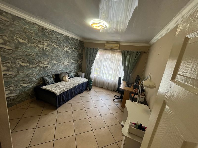 A bedroom featuring tiled flooring, crown molding, a wall-mounted air conditioning unit, and a decorative textured wallpaper feature wall.