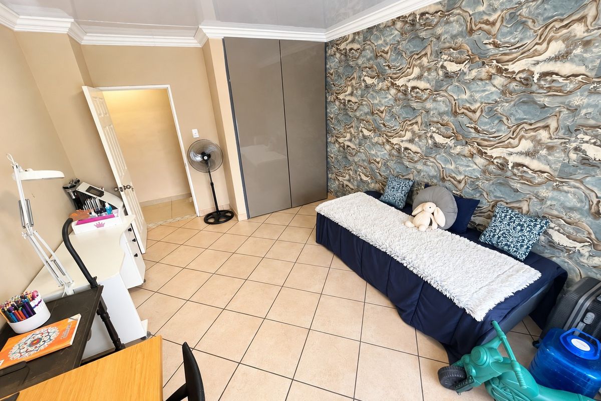 A bedroom featuring tiled flooring, built-in cupboards, and a decorative feature wall, offering a functional space with neutral wall tones.