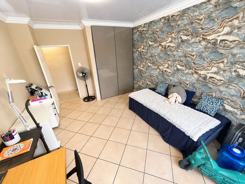 A bedroom featuring tiled flooring, built-in cupboards, and a decorative feature wall, offering a functional space with neutral wall tones.