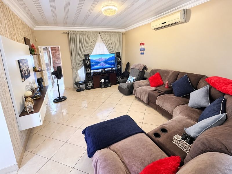 A spacious living room featuring tiled flooring, decorative ceiling molding, and a wall-mounted air conditioning unit, providing a comfortable and functional family space.