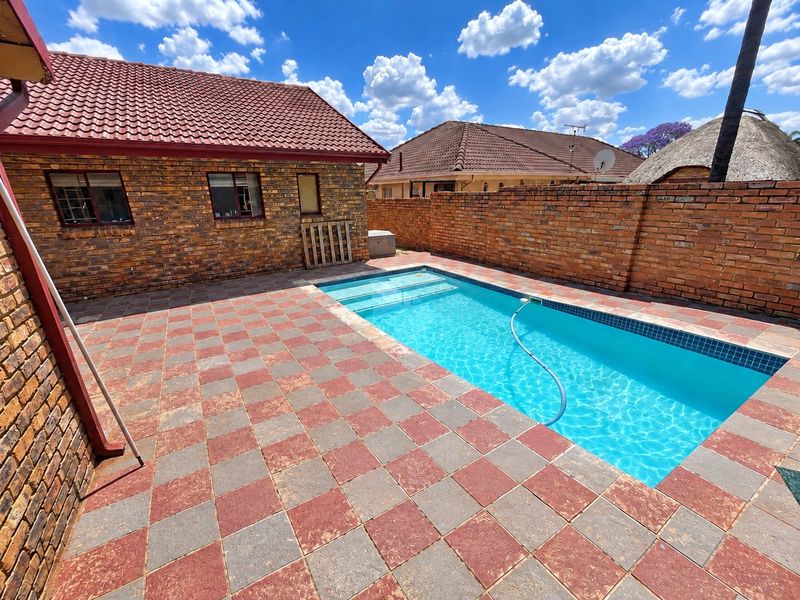 Outdoor pool area featuring a rectangular swimming pool, paved patio surround, and facebrick boundary walls.