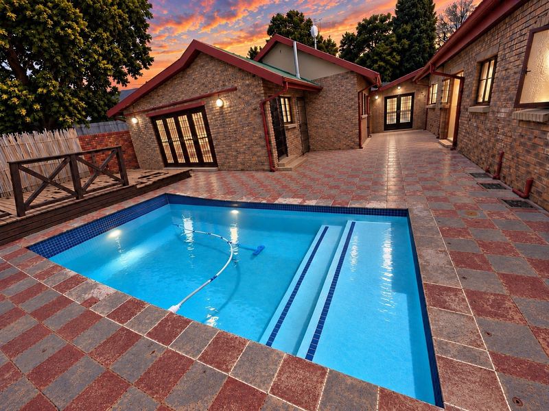 A well-maintained outdoor pool area featuring a tiled surround, timber decking, and direct access to the home via multiple sets of french doors.