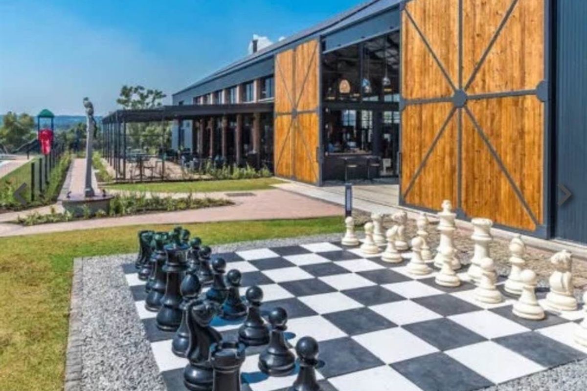 A well-maintained rear exterior featuring a large covered patio, expansive sliding timber doors, and a landscaped garden area with a permanent outdoor chess set.