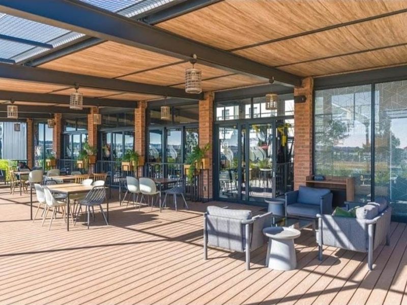 A spacious covered patio featuring timber decking, exposed brick columns, and a modern steel pergola structure with large glass sliding doors.
