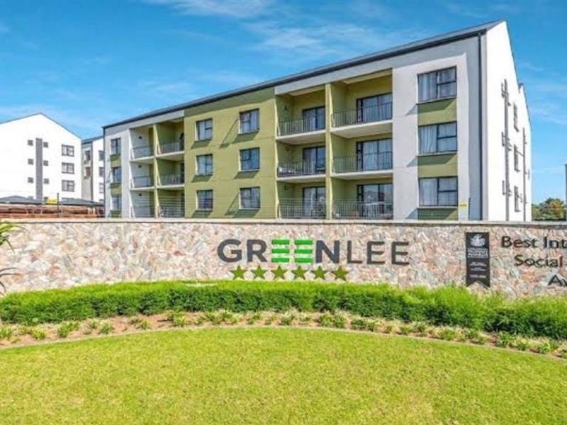 Front view of the Greenlee apartment complex featuring a stone-clad entrance wall, landscaped garden, and modern multi-story residential buildings with balconies.
