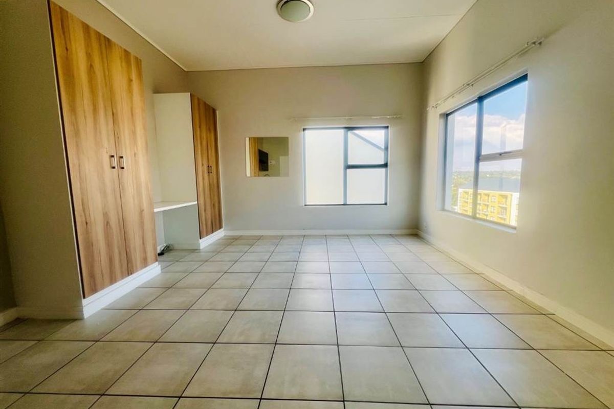 Spacious bedroom featuring neutral tiled flooring, built-in cupboards with a integrated desk, and large windows providing ample natural light.