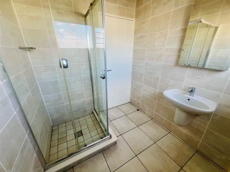 A clean and modern bathroom featuring a glass shower enclosure, pedestal basin, and neutral ceramic tiling throughout.