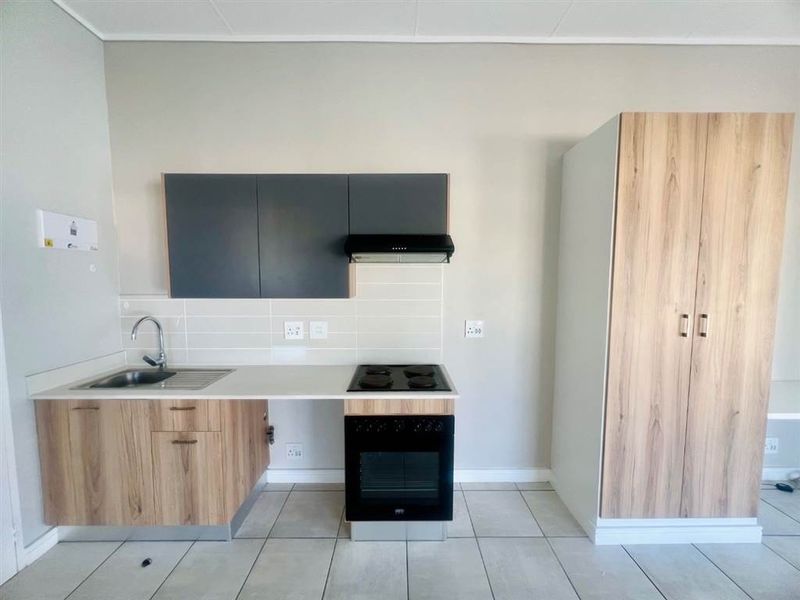Modern kitchen featuring wood-look cabinetry, built-in oven and hob, extractor fan, stainless steel sink, and neutral tiled flooring.