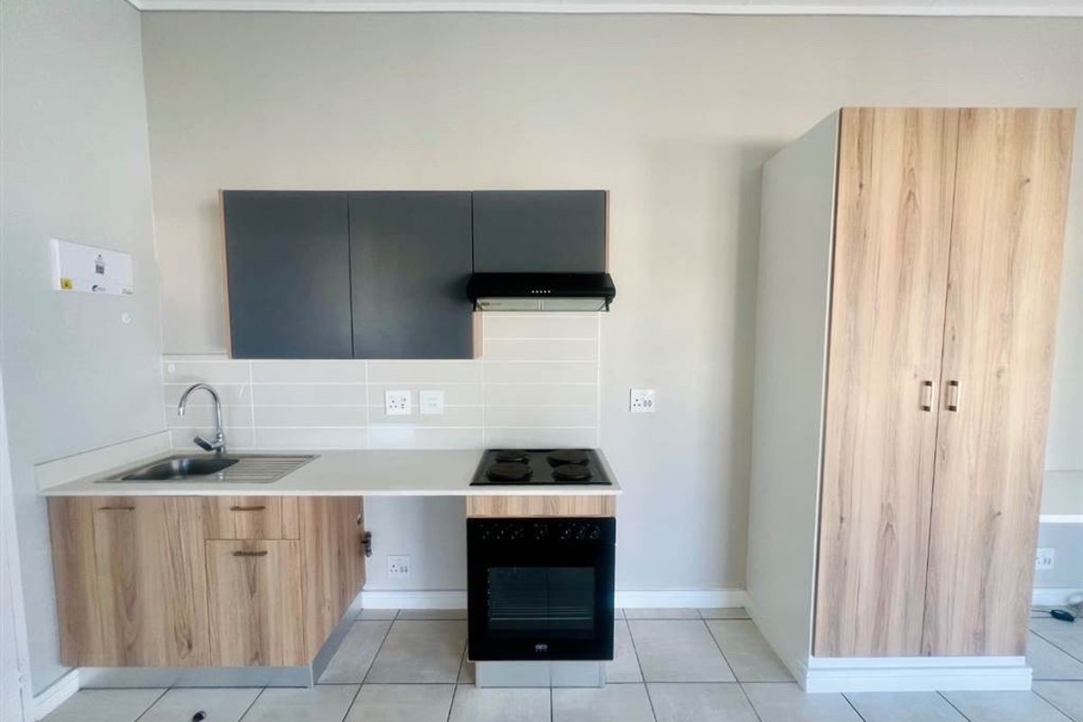Modern kitchen featuring wood-look cabinetry, built-in oven and hob, extractor fan, stainless steel sink, and neutral tiled flooring.