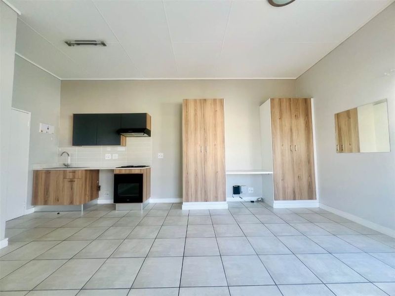 An open-plan living and kitchen area featuring modern built-in cabinetry, a hob, oven, extractor fan, and neutral tiled flooring throughout.