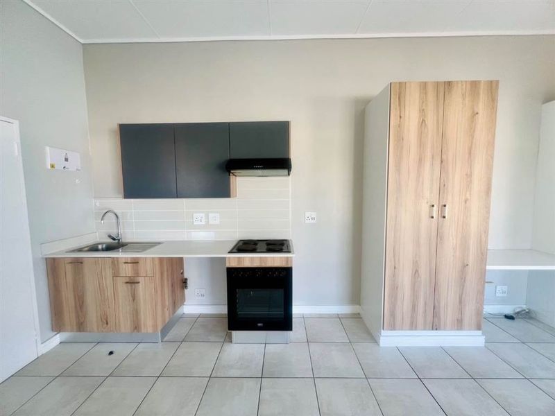 Modern kitchen featuring light wood-grain cabinetry, dark overhead cupboards, built-in oven and hob, extractor fan, and neutral tiled flooring.