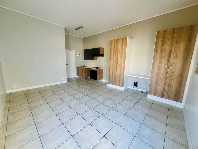 An open-plan living area featuring tiled floors, a compact kitchen with built-in cabinetry and appliances, and integrated storage cupboards.