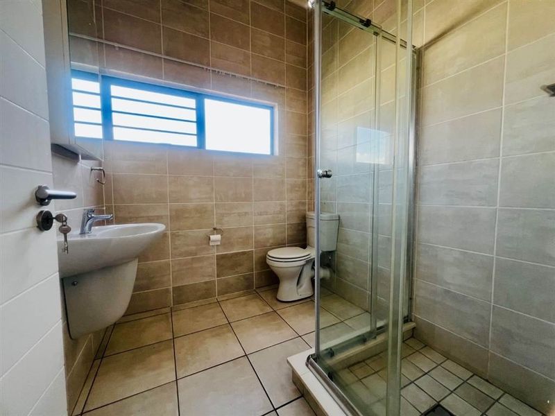 A functional bathroom featuring a glass shower enclosure, pedestal basin, and toilet with neutral wall and floor tiling.