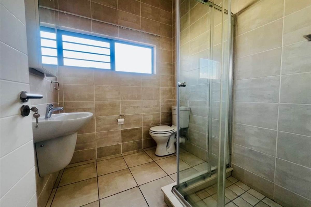 A functional bathroom featuring a glass shower enclosure, pedestal basin, and toilet with neutral wall and floor tiling.