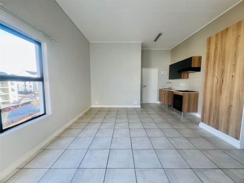 An open-plan living and kitchen area featuring modern tiled flooring, built-in cabinetry with integrated appliances, and a large window providing natural light.
