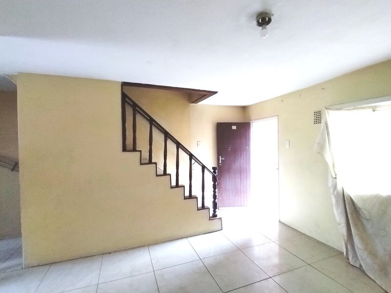 An empty living area featuring tiled flooring and a timber staircase, providing a blank canvas for potential interior updates.