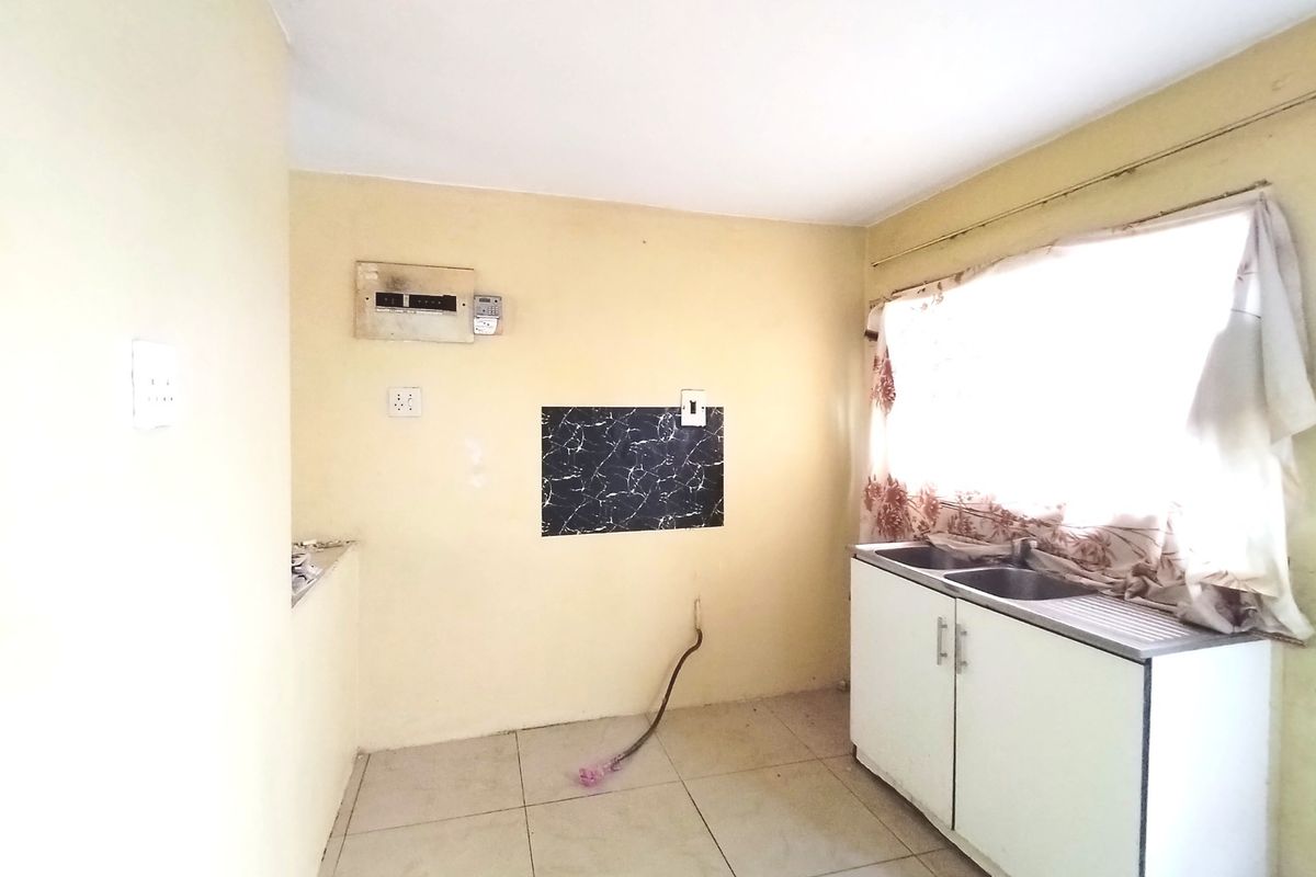 A functional kitchen space featuring a double bowl stainless steel sink, base cabinetry, and tiled flooring, ready for modernization and renovation.