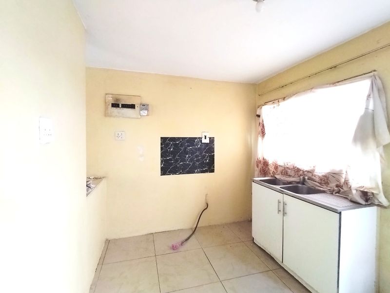 A functional kitchen space featuring a double bowl stainless steel sink, base cabinetry, and tiled flooring, ready for modernization and renovation.