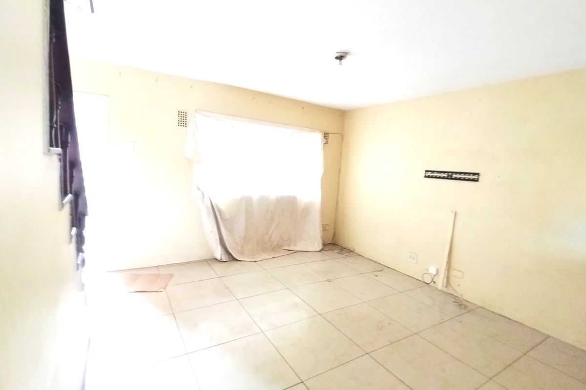 An empty living room featuring tiled flooring and neutral walls, requiring cosmetic updates to enhance its appeal.