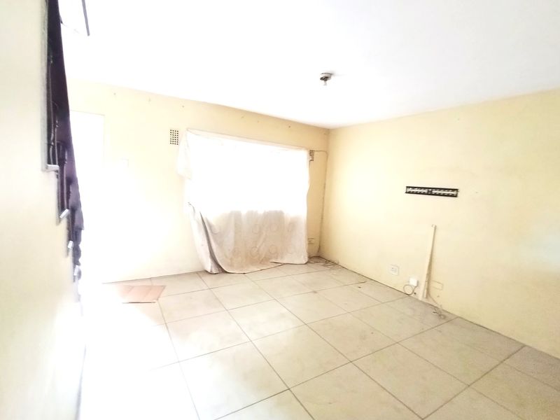 An empty living room featuring tiled flooring and neutral walls, requiring cosmetic updates to enhance its appeal.