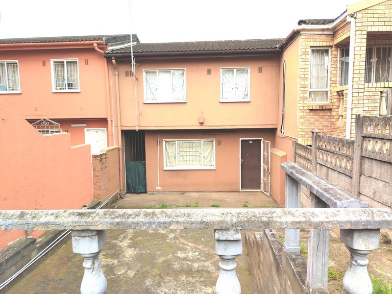 Rear view of a multi-story townhouse featuring a paved courtyard, concrete balustrade, and security-fitted doors and windows.