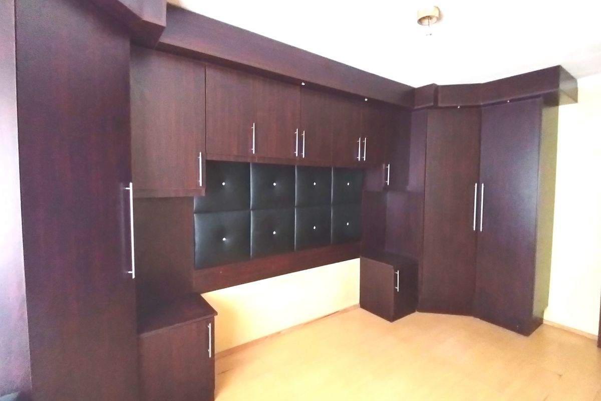 A bedroom featuring extensive dark wood built-in cabinetry with an integrated upholstered headboard panel and light-toned laminate flooring.