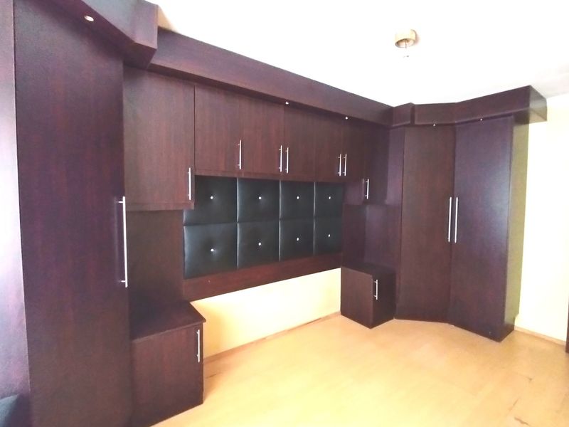 A bedroom featuring extensive dark wood built-in cabinetry with an integrated upholstered headboard panel and light-toned laminate flooring.