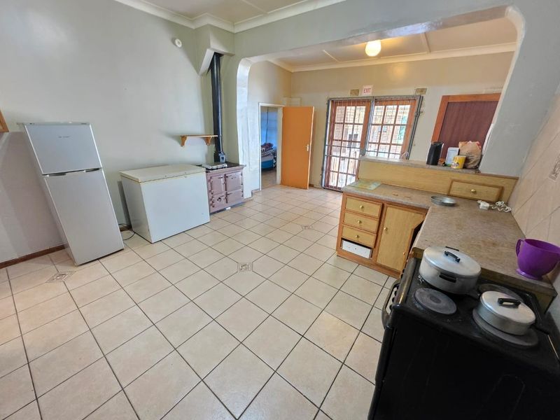 Open-plan kitchen and living area featuring tiled floors, built-in cabinetry, and a wood-burning stove, offering a functional layout with direct access to the exterior.