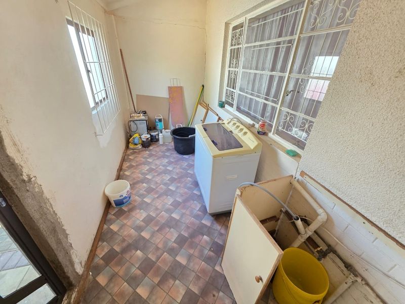 A functional laundry area featuring tiled flooring and security bars on windows, requiring some cosmetic updates to improve the overall finish.