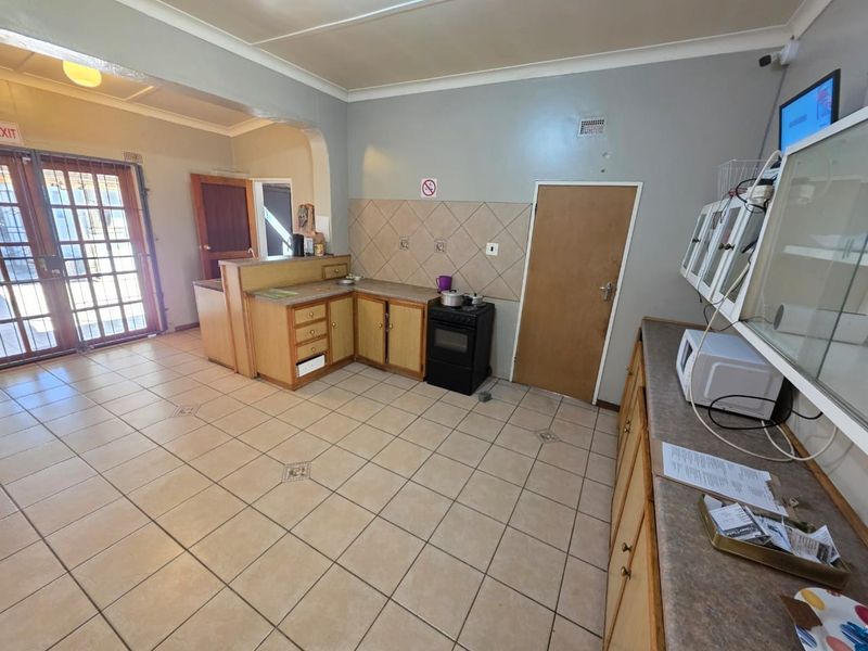 A functional kitchen featuring tiled flooring, built-in cabinetry with laminate countertops, a freestanding stove, and a tiled splashback, with direct access to an exterior door.