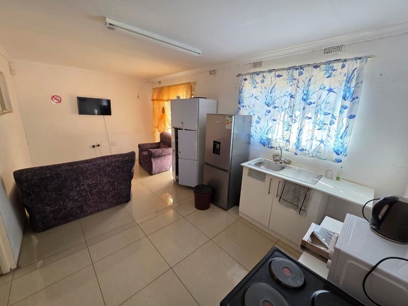 Open plan living area featuring tiled flooring and a compact kitchen with basic cabinetry, sink, and electric hob.