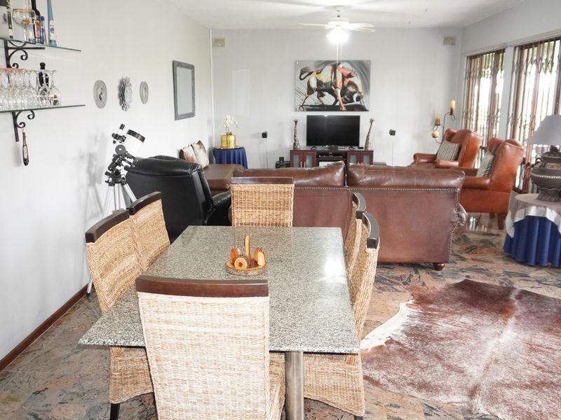 Spacious open-plan living and dining area featuring stone flooring, a ceiling fan, and large windows with security gates.
