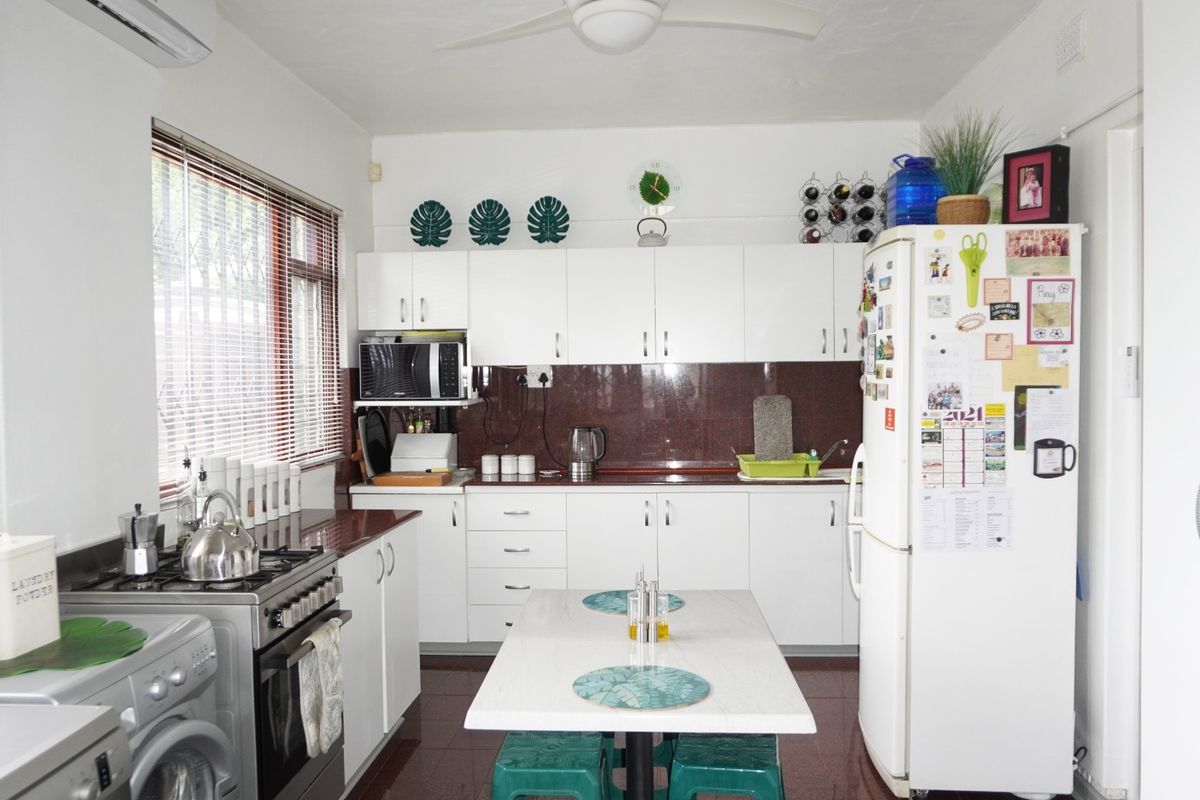 A functional kitchen featuring white cabinetry, a gas stove with oven, tiled splashback, and integrated appliances, offering a clean and practical workspace.