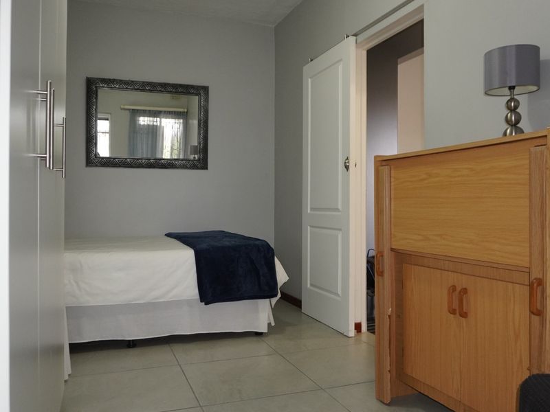 A well-maintained bedroom featuring neutral grey walls, tiled flooring, and a built-in wardrobe, offering a clean and functional living space.