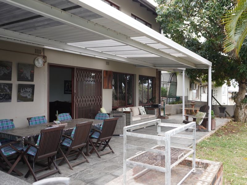 A spacious covered patio featuring paved flooring and a built-in brick braai, providing an ideal outdoor entertainment area overlooking the garden.