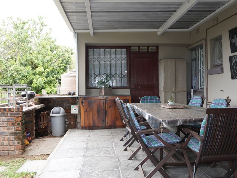 A covered outdoor patio featuring a built-in brick braai, tiled flooring, and integrated wooden cabinetry, providing a functional space for outdoor dining and entertainment.
