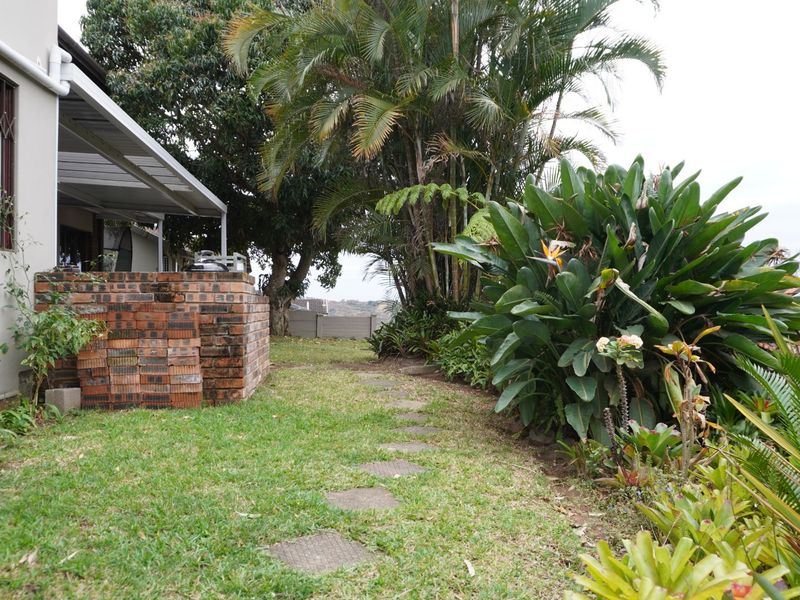 Rear garden area featuring a covered patio, established landscaping, and a brick built-in braai structure.