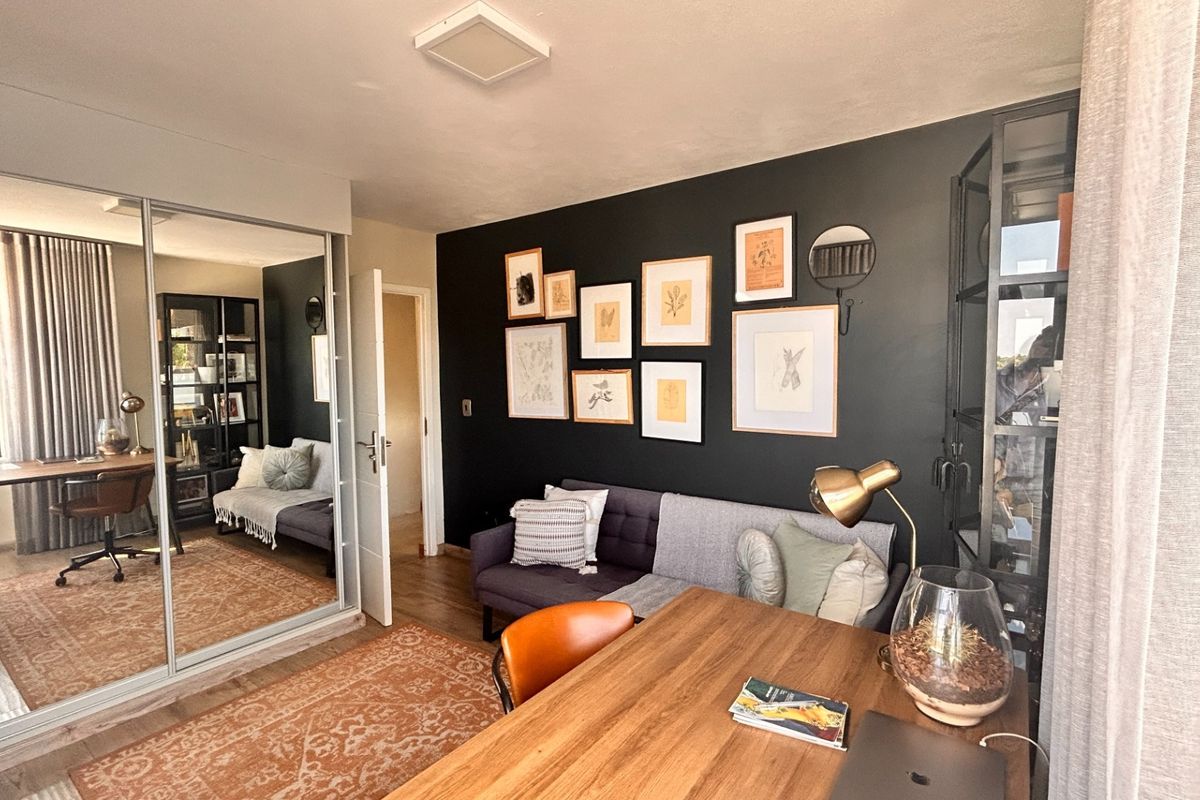 A well-maintained bedroom featuring large mirrored sliding wardrobe doors, laminate flooring, and a contemporary dark accent wall.