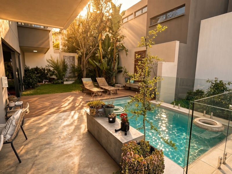 A modern outdoor entertainment area featuring a swimming pool with glass balustrades, timber decking, and a landscaped garden setting.
