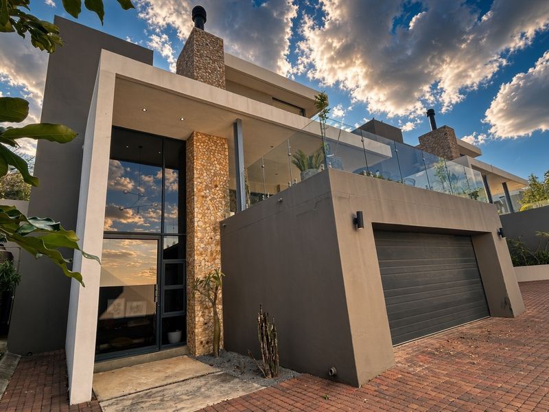 Modern townhouse exterior featuring stone cladding, a glass-railed balcony, and a double garage, showcasing contemporary architectural design and high-quality finishes.