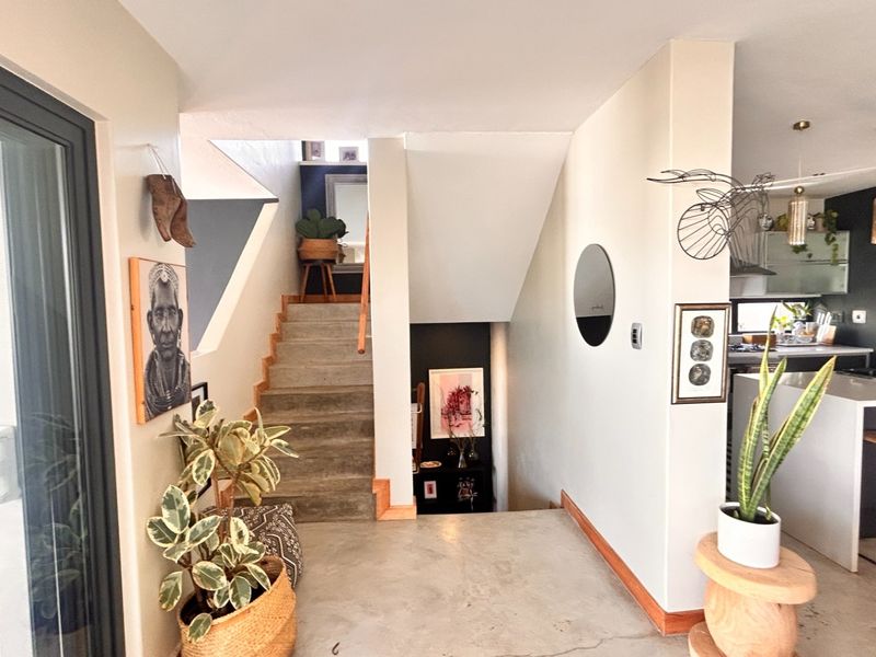 An open-plan living area featuring a modern staircase, polished concrete flooring, and a contemporary kitchen with a central island and pendant lighting.