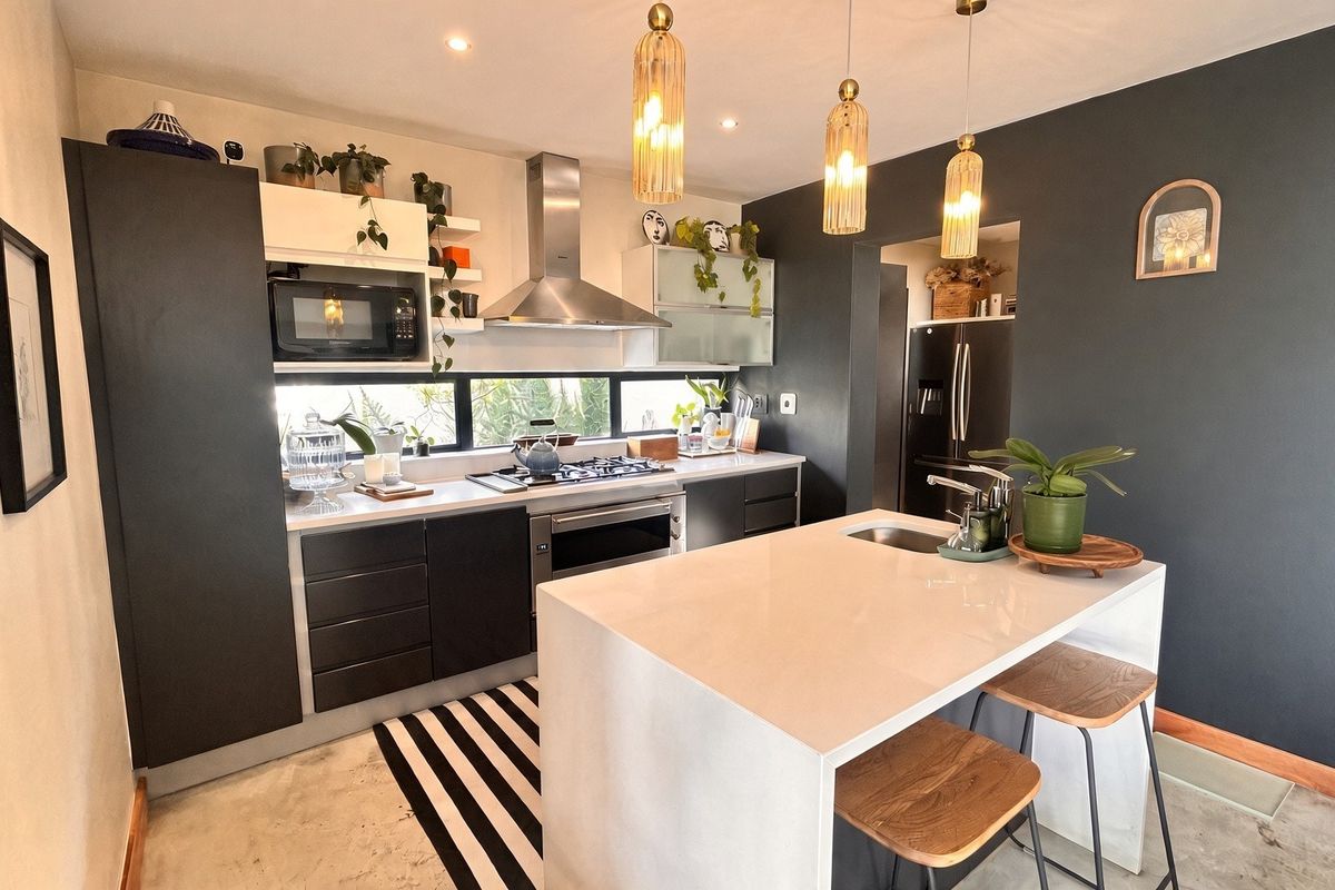 Modern kitchen featuring dark cabinetry, stone countertops, a central island with seating, and high-quality built-in appliances including a gas hob and extractor fan.